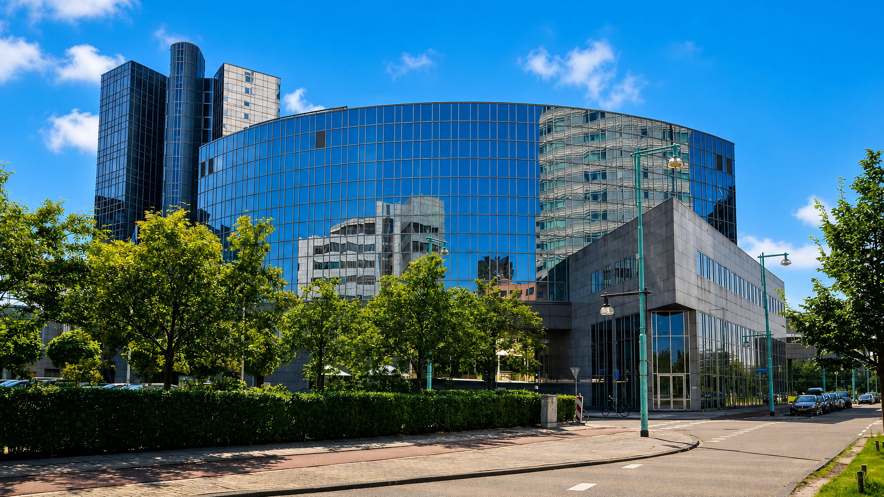 Curved blue-glass and dark office towers along a quiet street in Amsterdam's Sloterdijk business district.