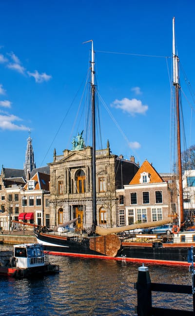 Sailing ship moored on Haarlem's Spaarne river beside the Teylers Museum, with the Grote Kerk tower beyond.