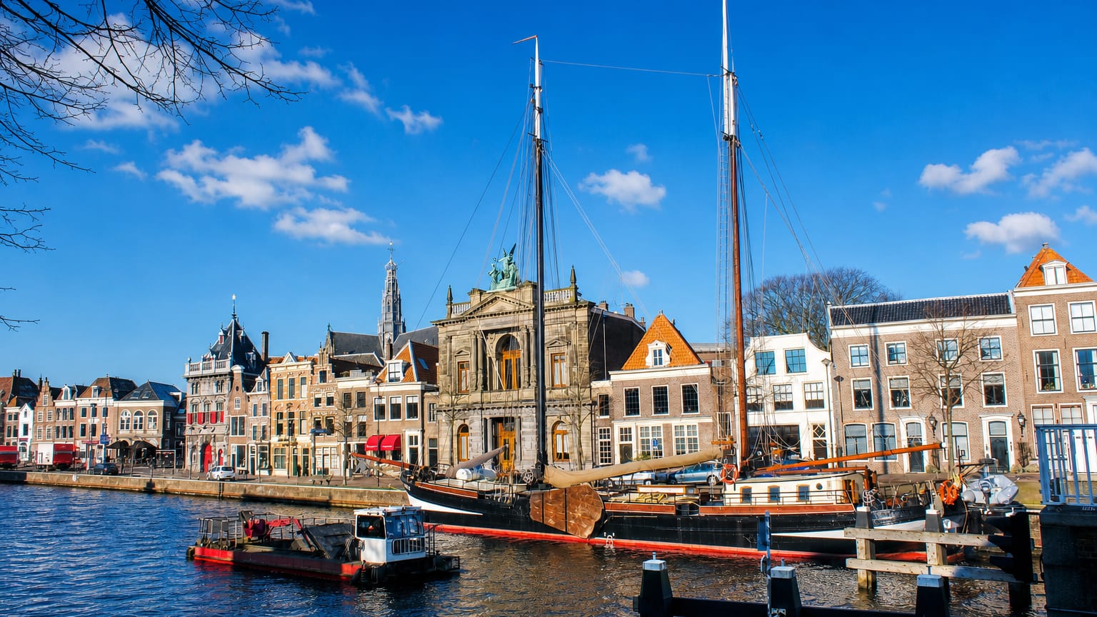 Sailing ship moored on Haarlem's Spaarne river beside the Teylers Museum, with the Grote Kerk tower beyond.