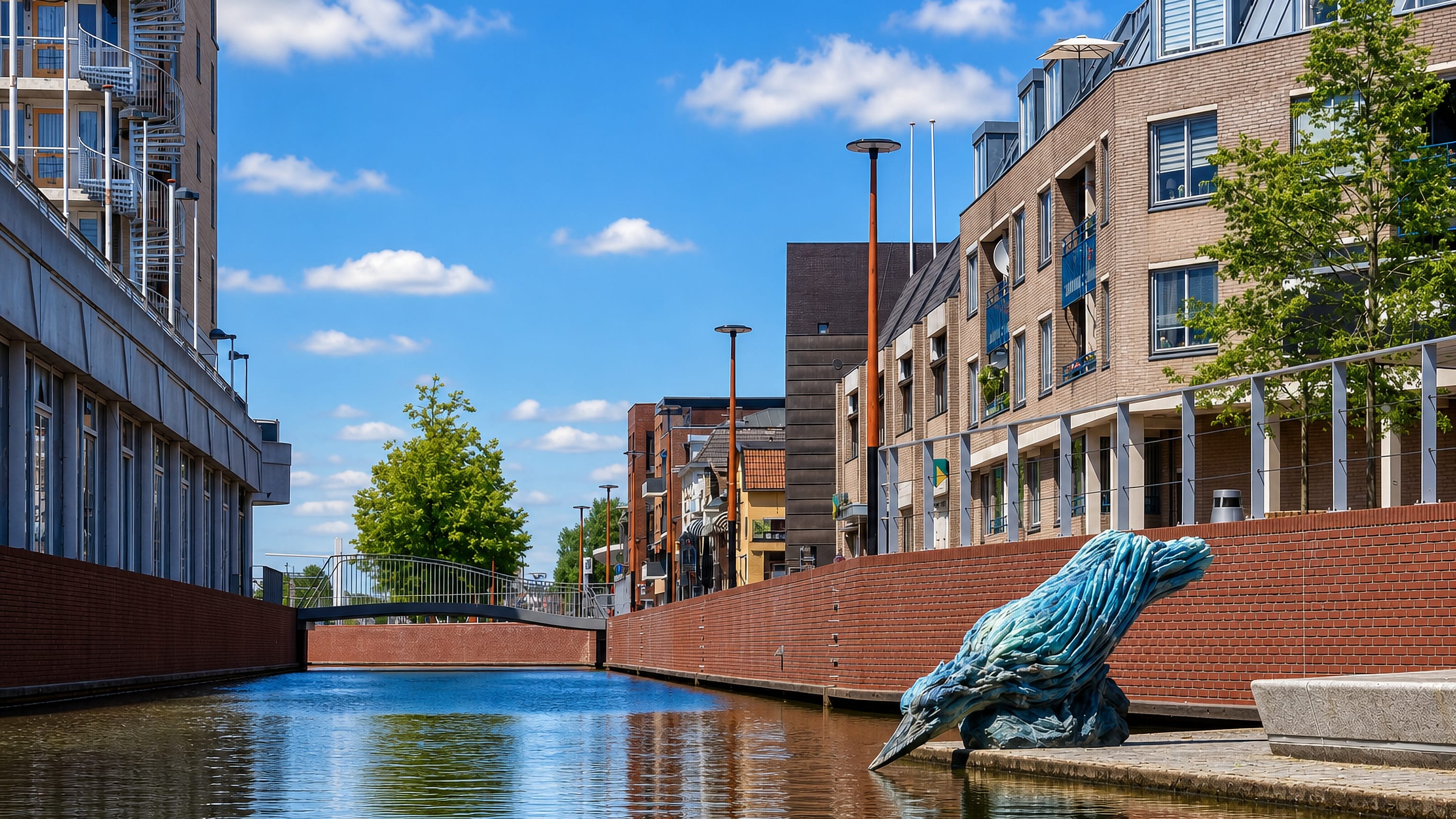 Canal lined with modern brick apartments and a wave-like sculpture in Almelo, Netherlands.