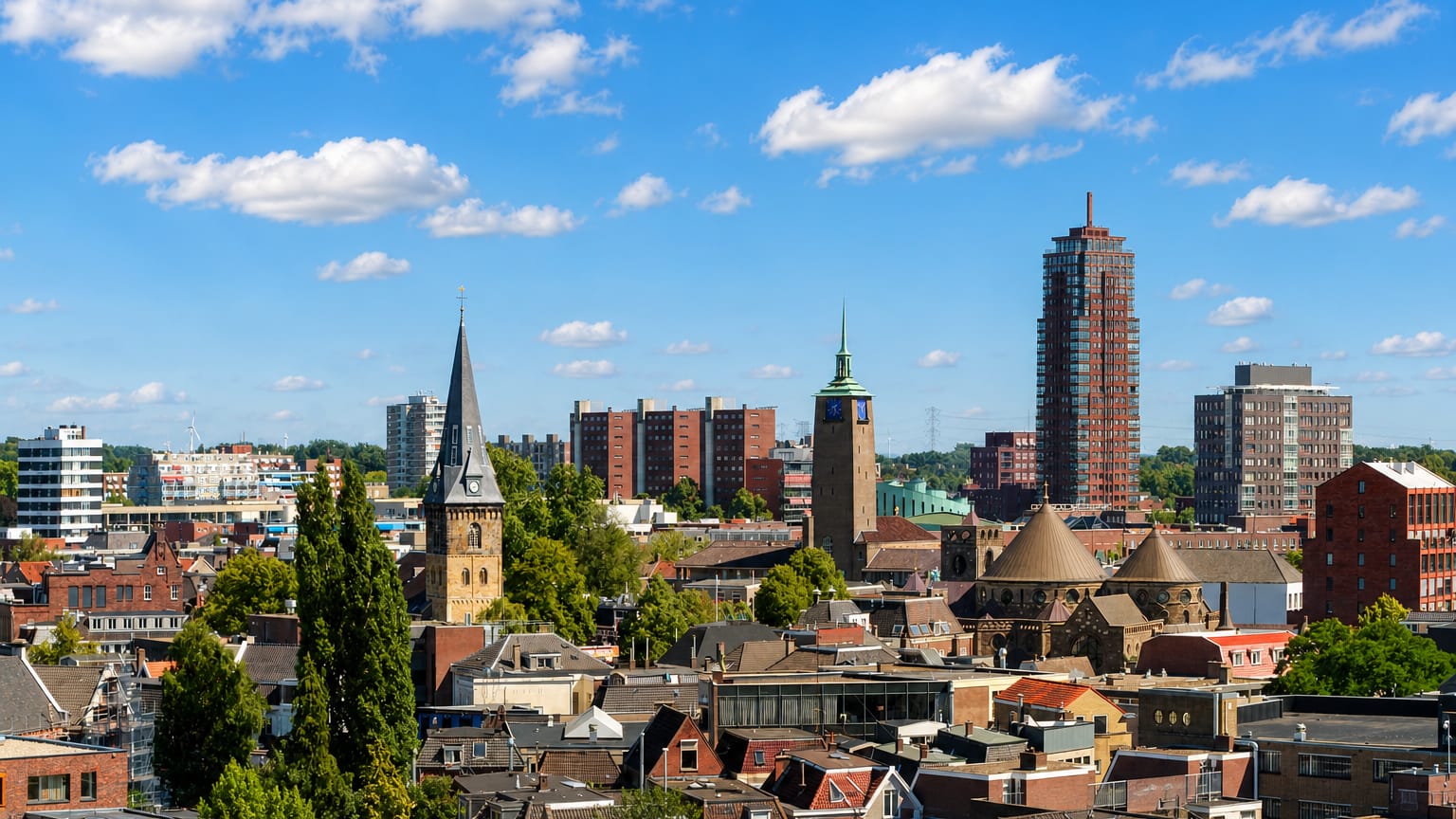Enschede's skyline with a church spire, a domed church and a modern tower above old rooftops.