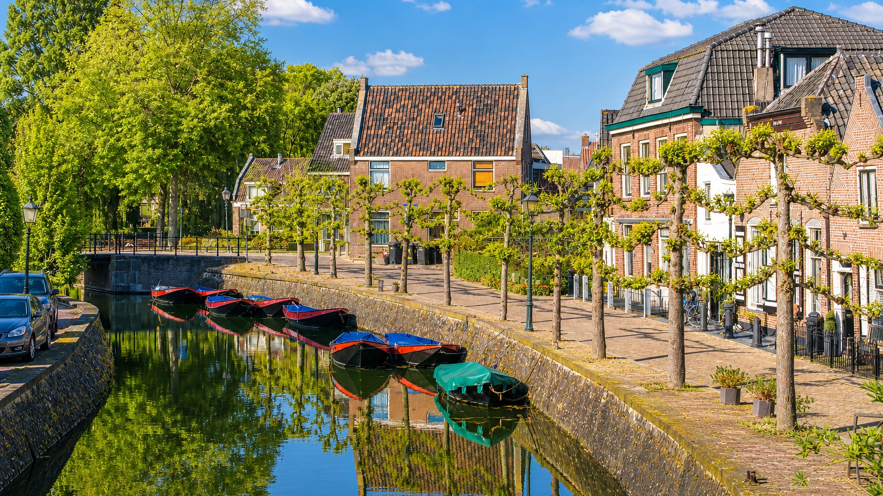 Moored flat-bottomed boats on a tree-lined canal beside brick houses in Vreeswijk, Nieuwegein.