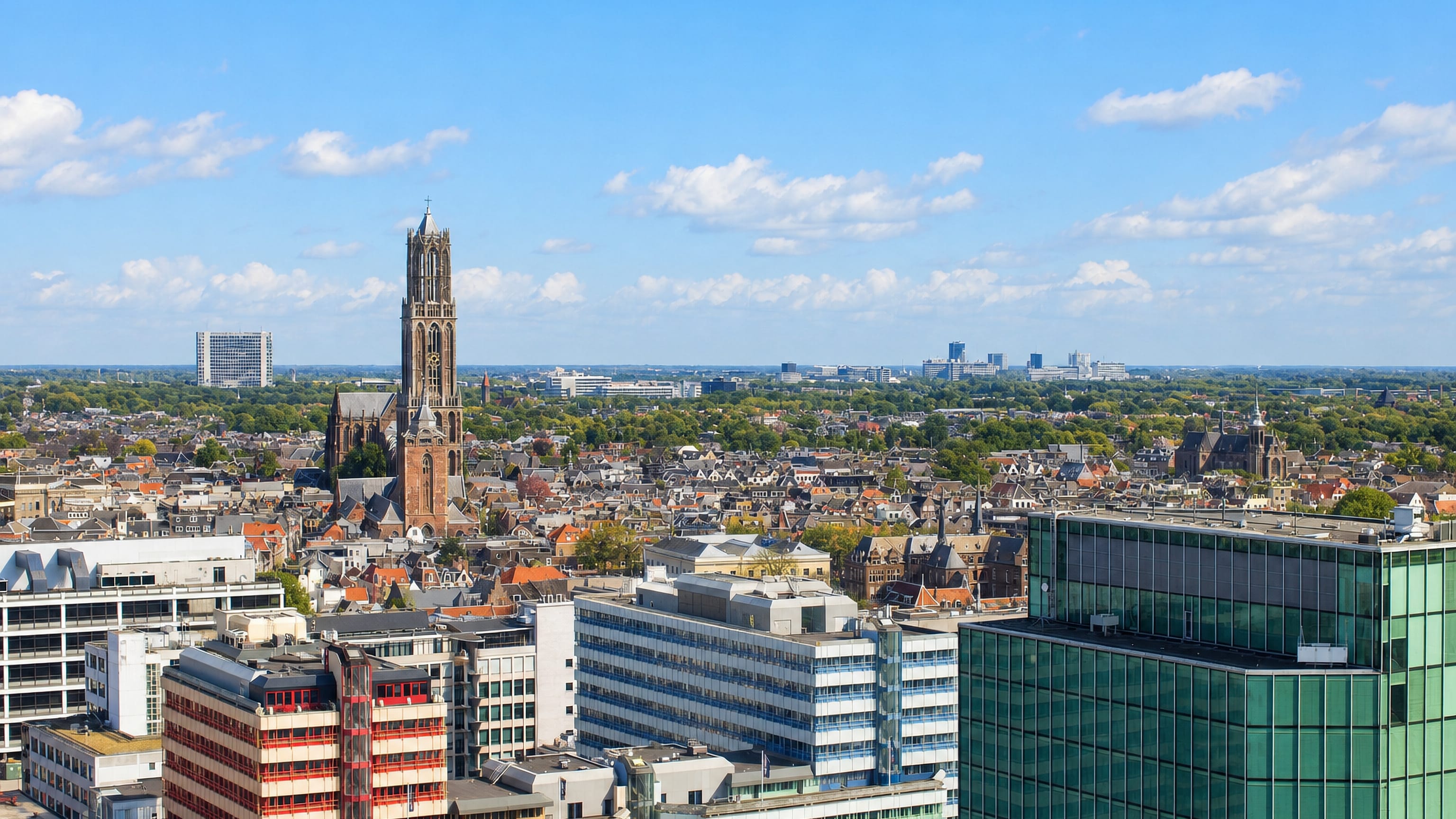 Utrecht's Dom Tower rising above city rooftops and modern offices, seen from the Tolsteeg side of the city.