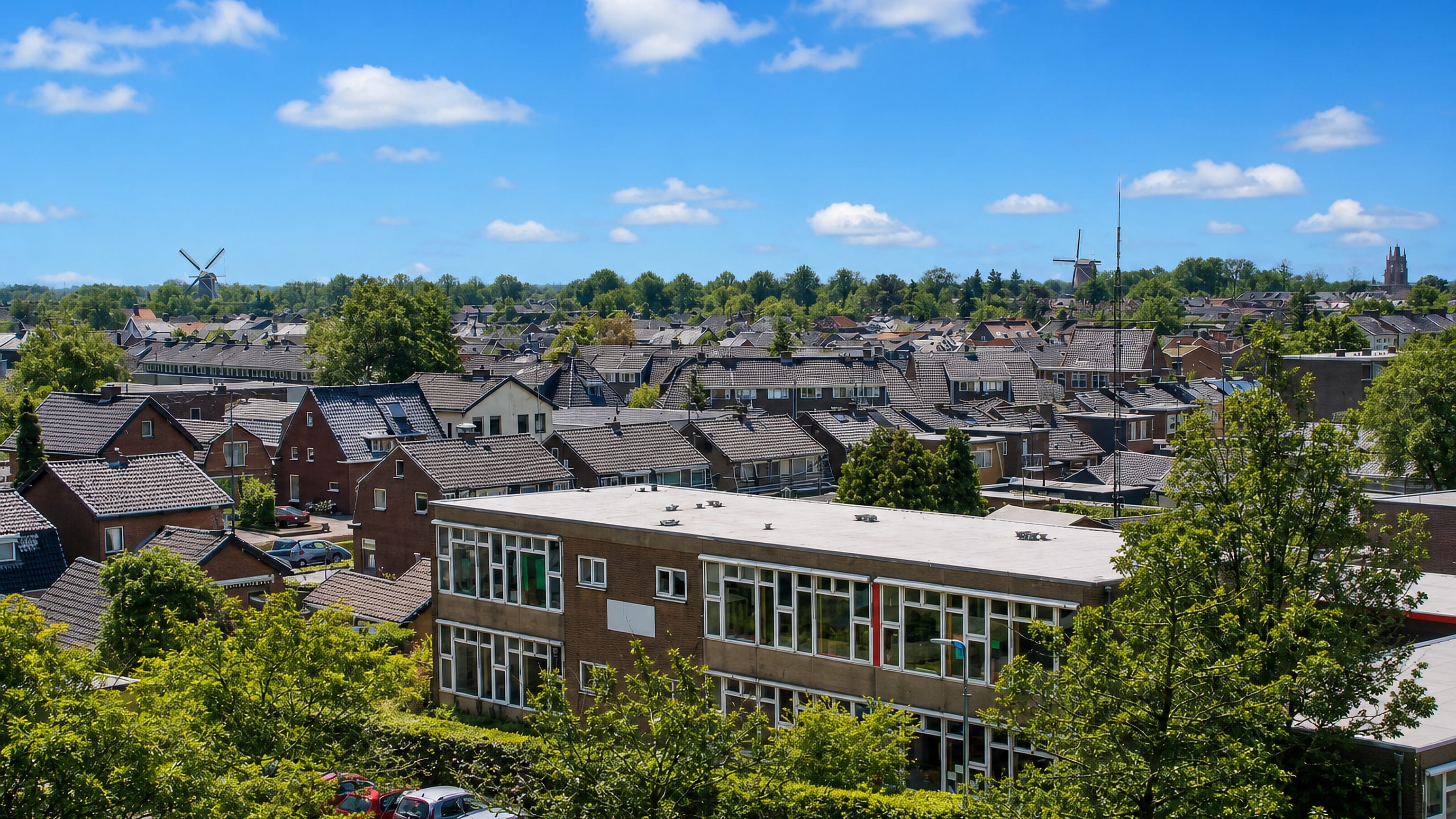 Brick houses and tiled roofs of Veenendaal under a summer sky, with two windmills on the skyline.