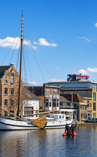 Historic sailing barge and a red-sailed yacht on a canal lined with Dutch houses in Delft.