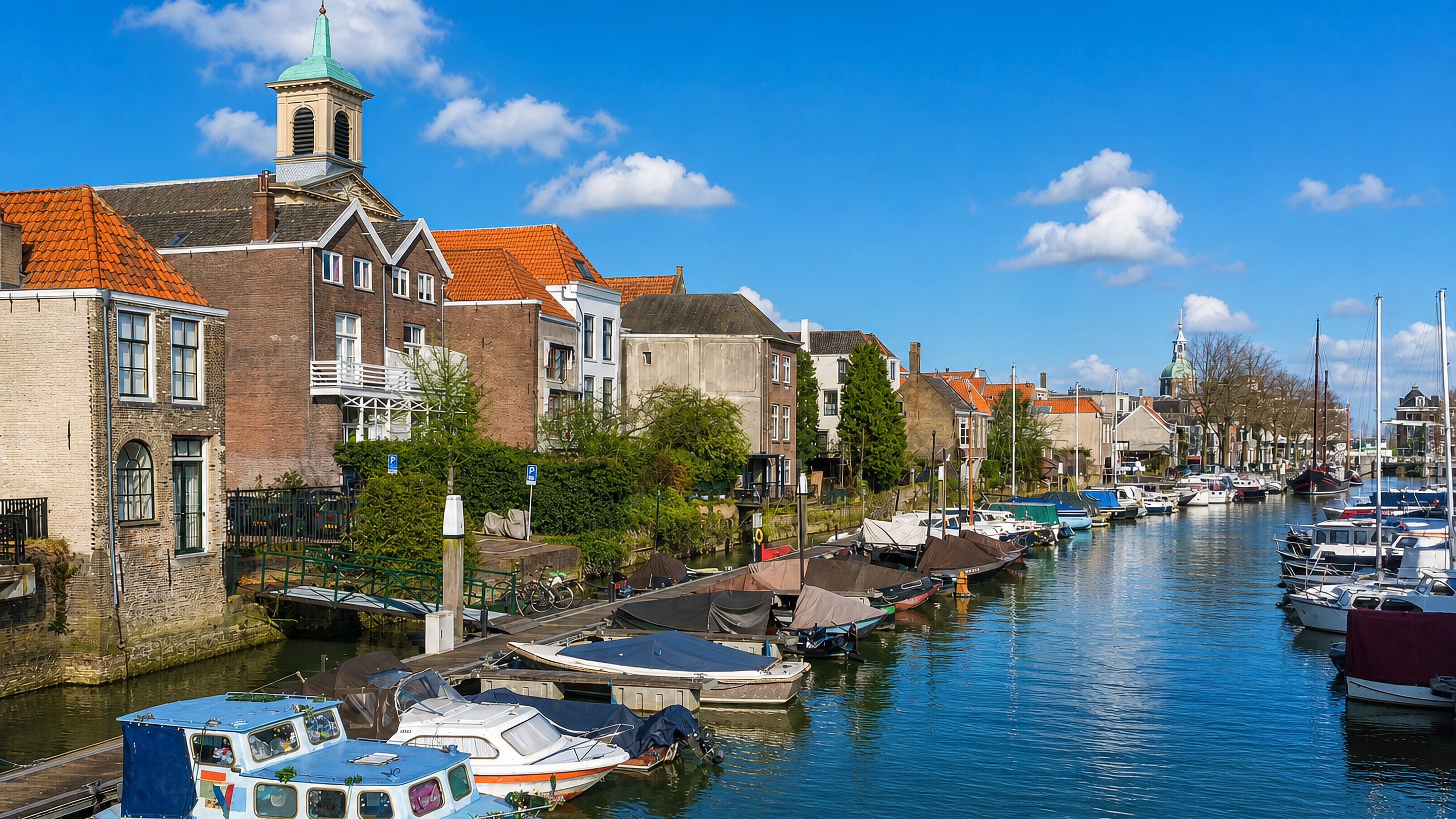 Dordrecht's old harbour with moored boats, gabled brick houses and a domed church tower beyond.
