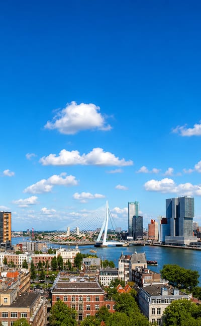 Rotterdam skyline with the Erasmusbrug and Kop van Zuid high-rises along the Nieuwe Maas river on a bright day.