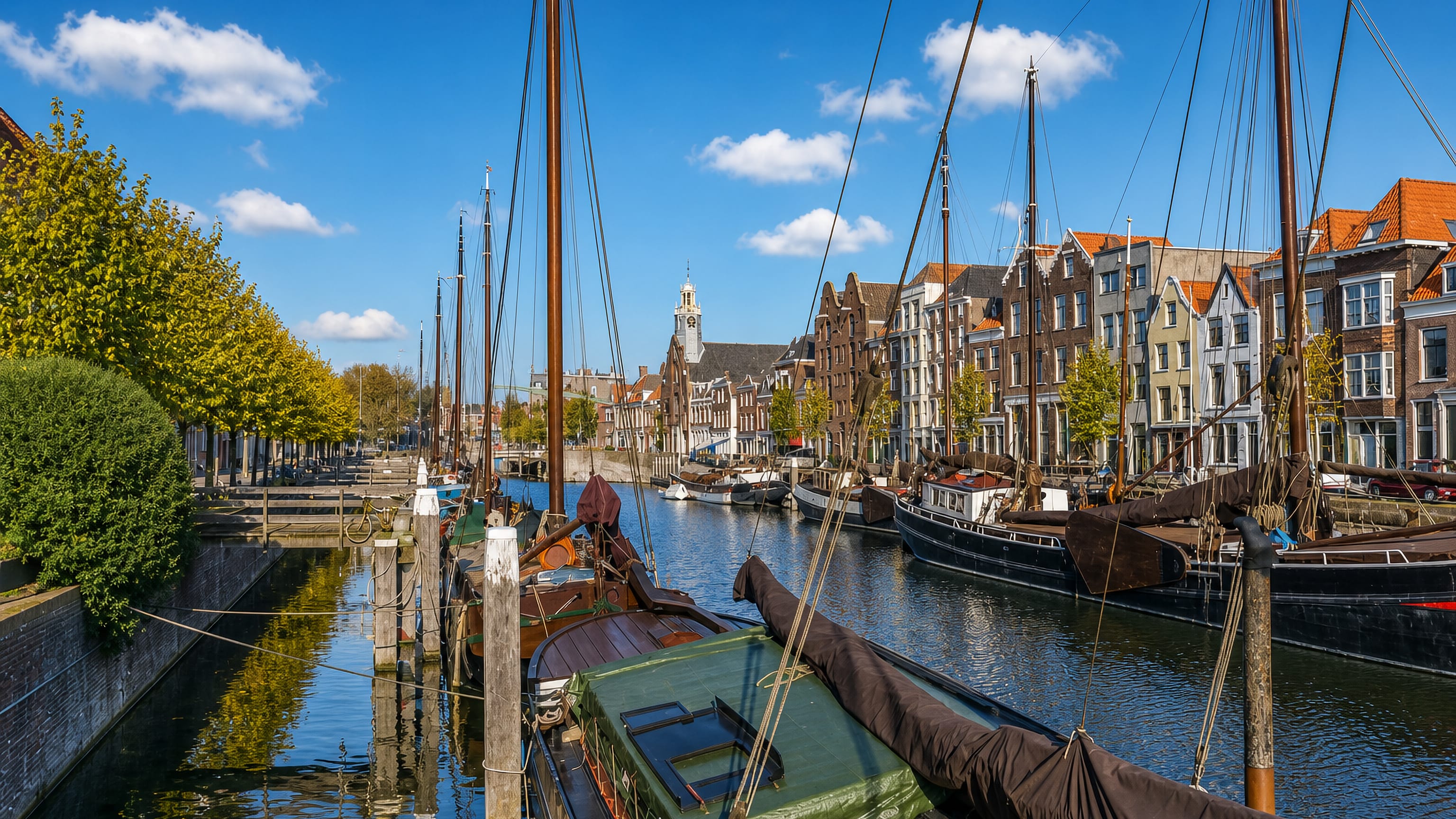 Historic sailing barges moored in Delfshaven's harbour, Rotterdam, lined with gabled houses and a white church tower.