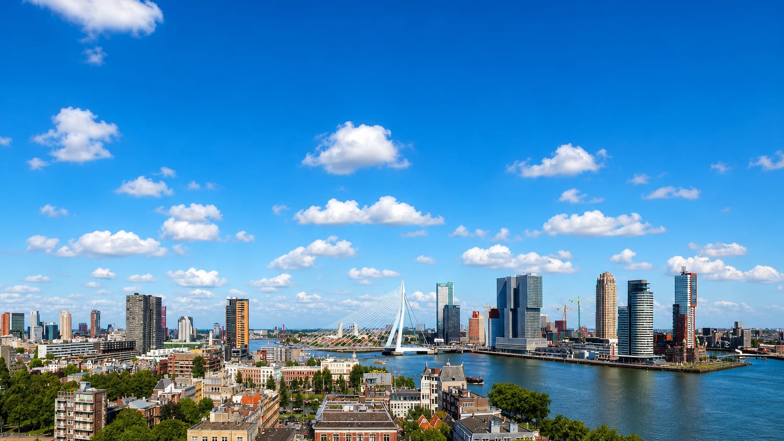 Rotterdam skyline with the Erasmusbrug and Kop van Zuid high-rises along the Nieuwe Maas river on a bright day.