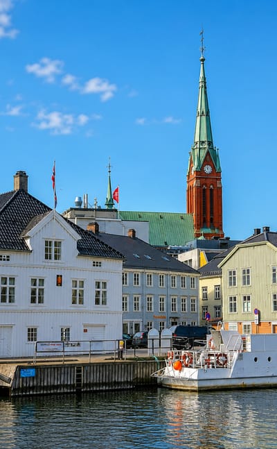 Arendal's waterfront with white timber houses, a moored ferry and the red-brick Trinity Church spire, Norway