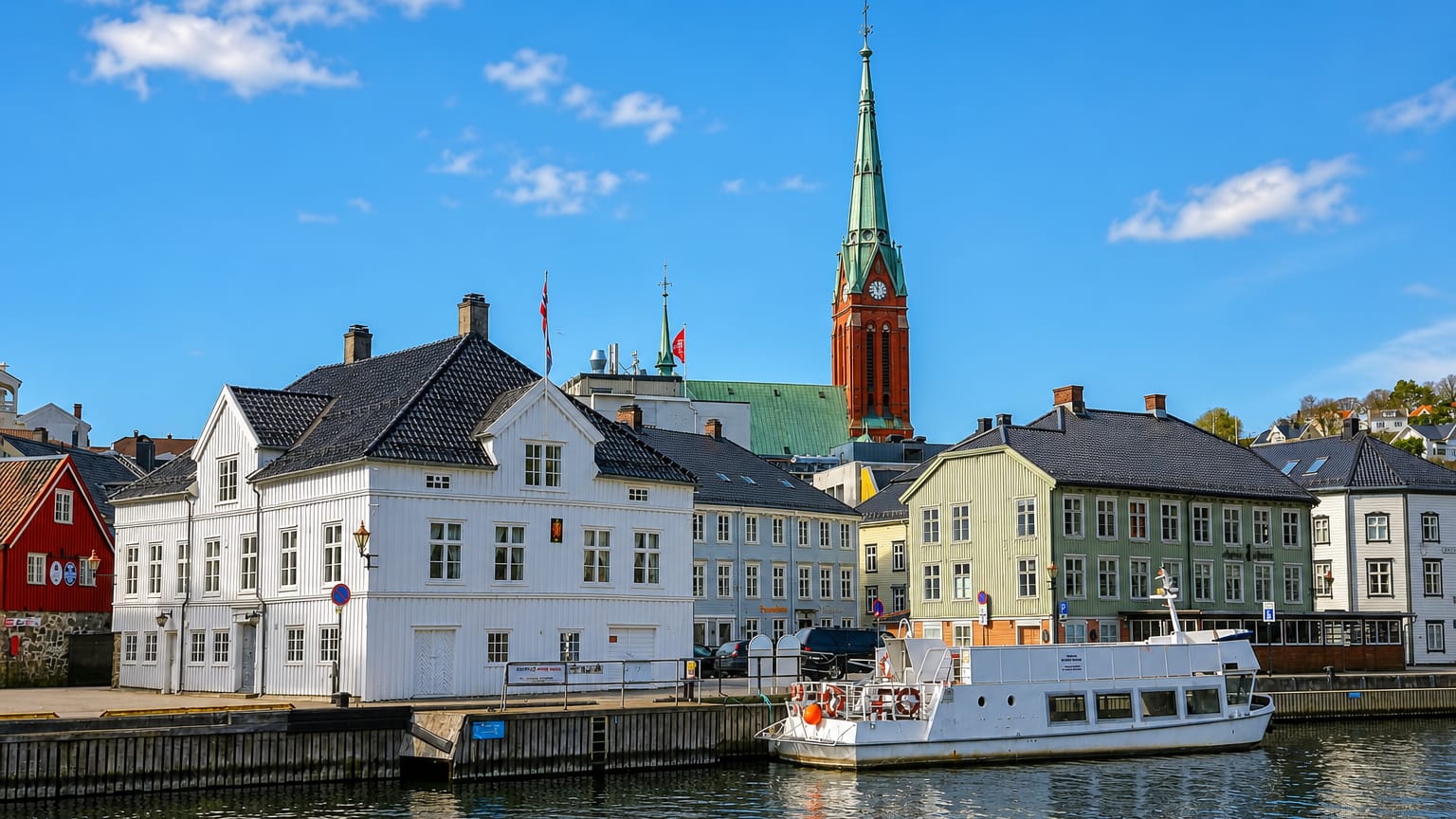 Arendal's waterfront with white timber houses, a moored ferry and the red-brick Trinity Church spire, Norway