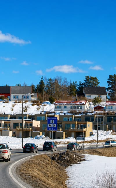 Winter roadside view of Birkeland, Norway, with modern townhouses on a snowy hillside and a place-name road sign.