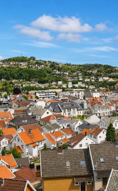 Elevated view over Flekkefjord's white wooden houses and orange-tiled roofs toward the fjord and forested hills