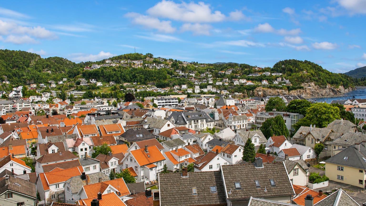 Elevated view over Flekkefjord's white wooden houses and orange-tiled roofs toward the fjord and forested hills