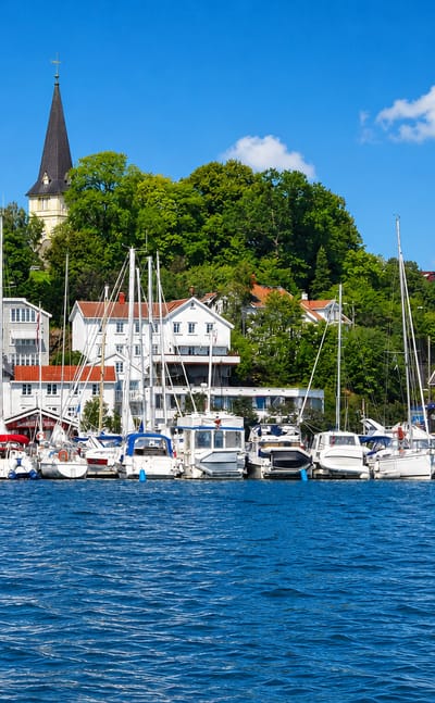 Grimstad's marina full of white sailing boats below white timber houses and a church spire on a wooded hill