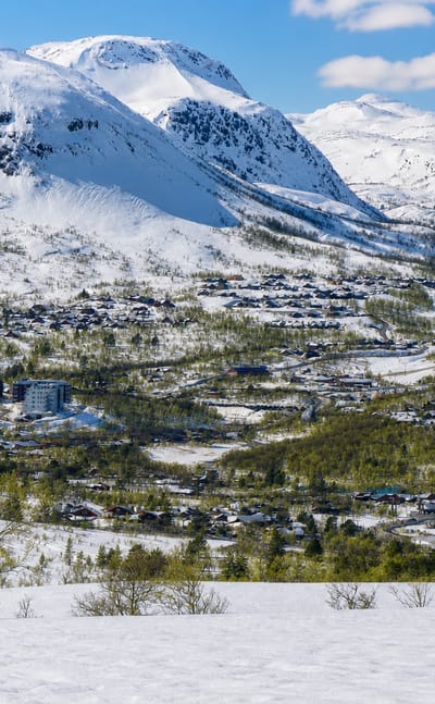 Snow-capped fells rising above the alpine ski village of Hovden, Norway, with scattered cabins and hotels across the valley.