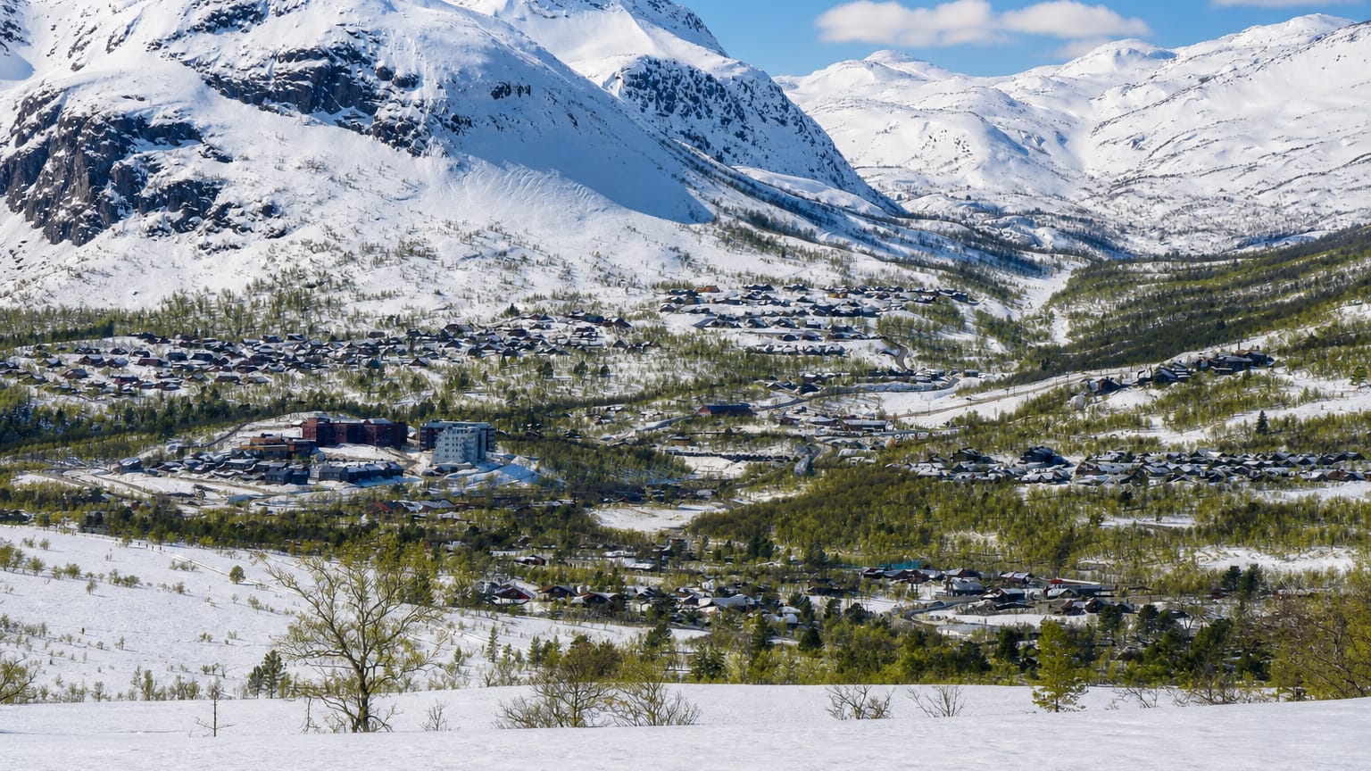 Snow-capped fells rising above the alpine ski village of Hovden, Norway, with scattered cabins and hotels across the valley.