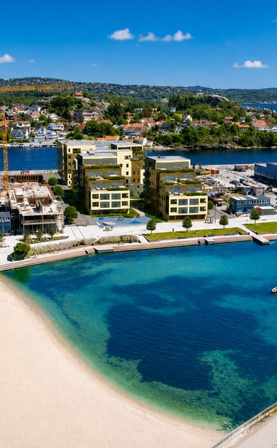 Aerial view of Kristiansand's city beach with turquoise water, a marina and modern waterfront buildings