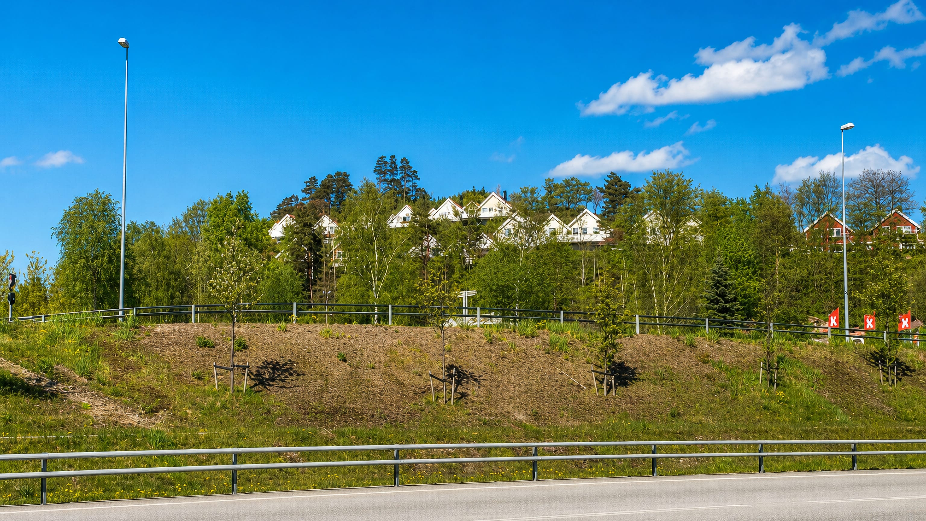 White houses on a wooded ridge above a roadside embankment in Hånes, Kristiansand.