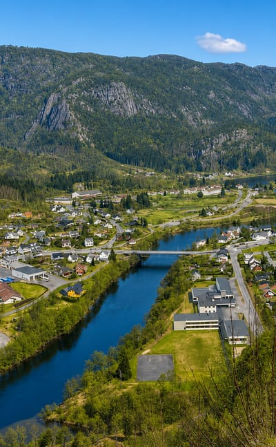 Elevated view of Liknes along the Kvina river with a road bridge and mountains behind