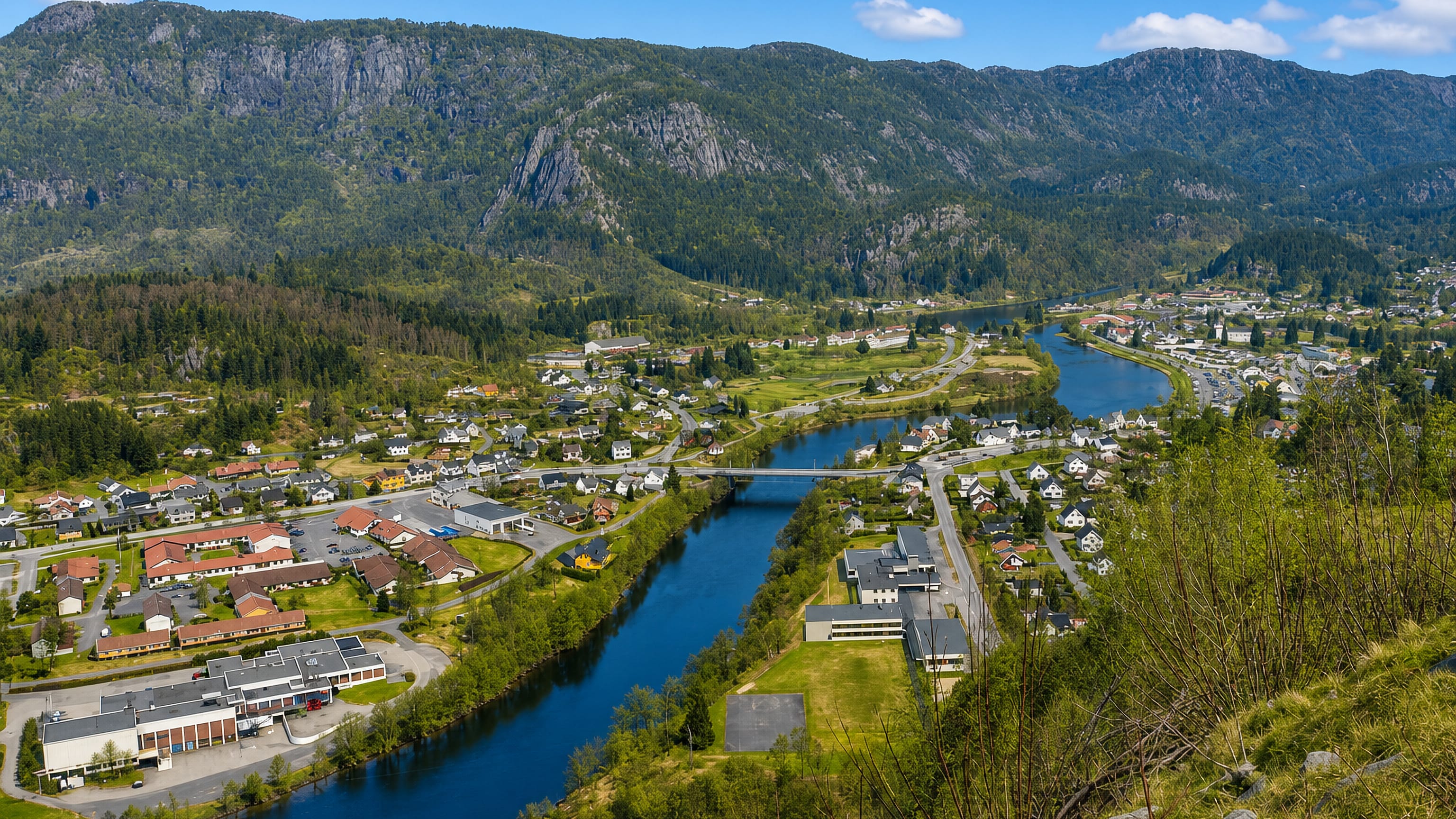 Elevated view of Liknes along the Kvina river with a road bridge and mountains behind