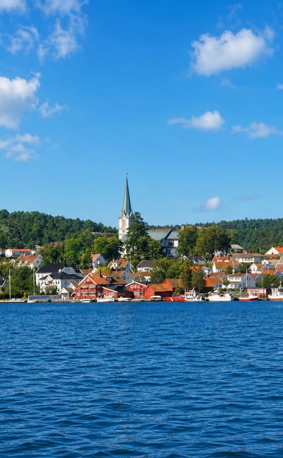 White timber houses and a church spire along the waterfront of Lillesand, Norway