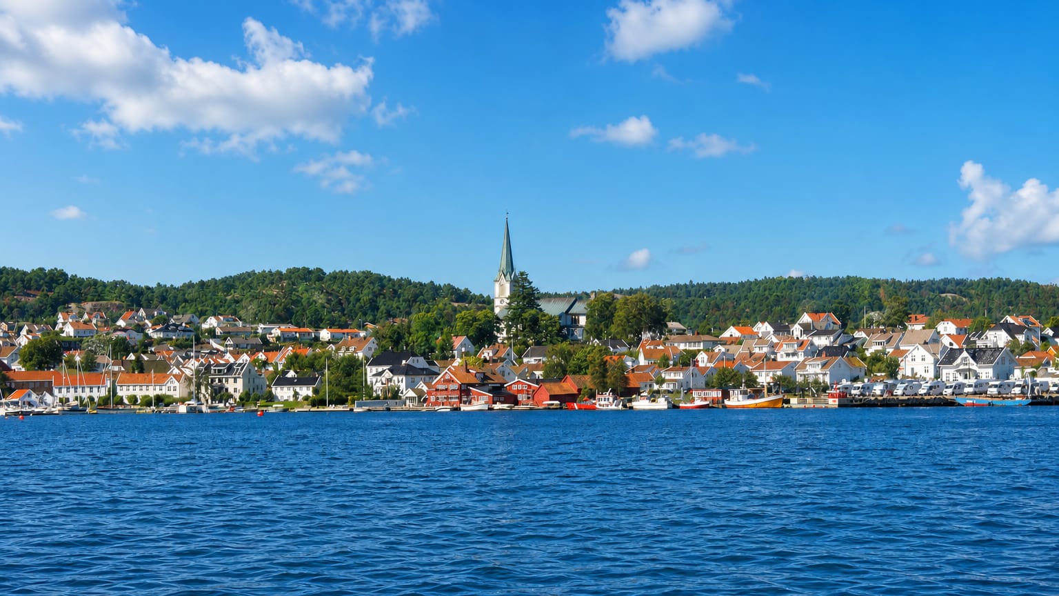 White timber houses and a church spire along the waterfront of Lillesand, Norway