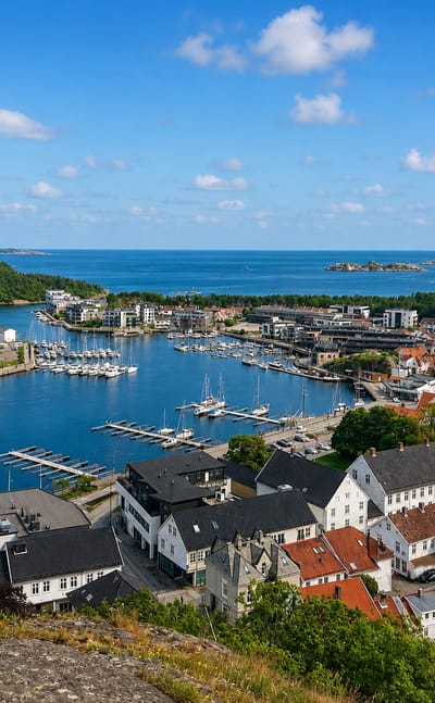 Elevated view over Mandal's harbour and marina on the Mandalselva with white wooden houses and the coast beyond.