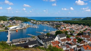Elevated view over Mandal's harbour and marina on the Mandalselva with white wooden houses and the coast beyond.