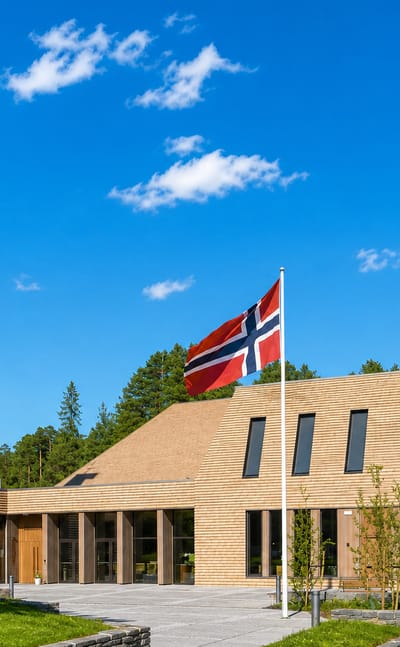 Modern timber-clad church with a tall pyramidal bell tower and Norwegian flag in Vennesla