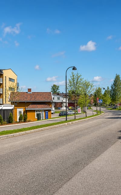 Quiet suburban street with apartment blocks, a yellow timber house and roadside trees in Ask, Gjerdrum, Norway.