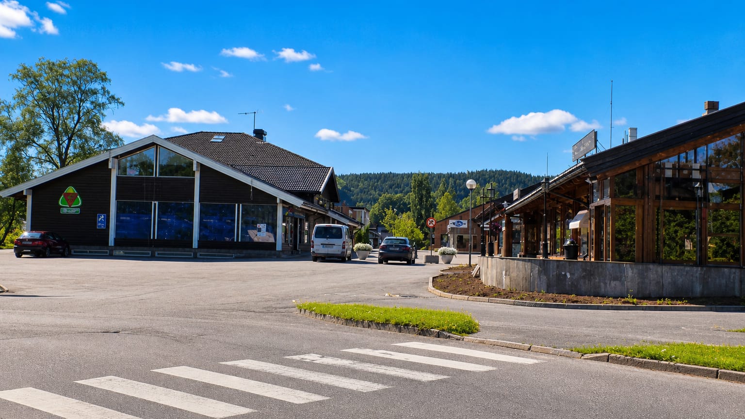 The wood-clad village centre of Bjørkelangen with a pedestrian crossing and forested hills behind.
