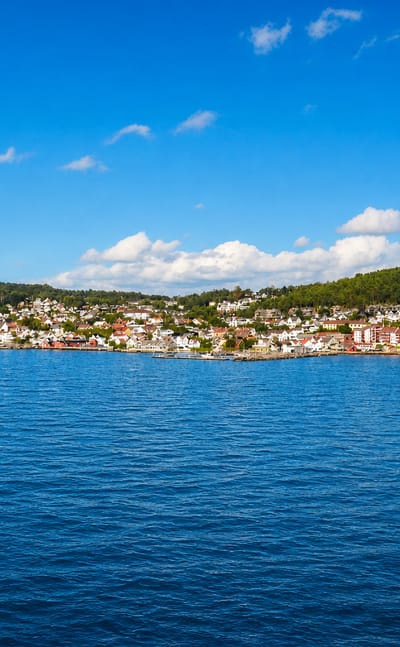 Distant view of Drobak, Norway, along the wooded Oslofjord shore across a broad expanse of blue water