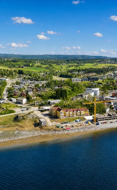 Aerial daytime view of Eidsvoll, Norway, a riverside town along the Vorma with low-rise buildings, a bridge and wooded green hills