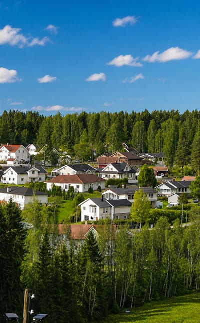White and red houses nestled in green birch and conifer forest under a blue summer sky in Jessheim, Norway