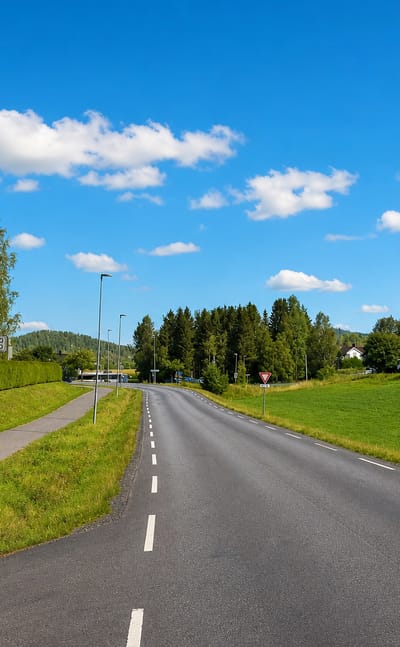An empty rural road with an Enebakk signpost and green fields near Kirkebygda, Norway.