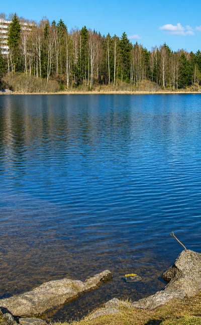 A calm forest-ringed lake with a white apartment block on the hillside at Kjenn, Norway.