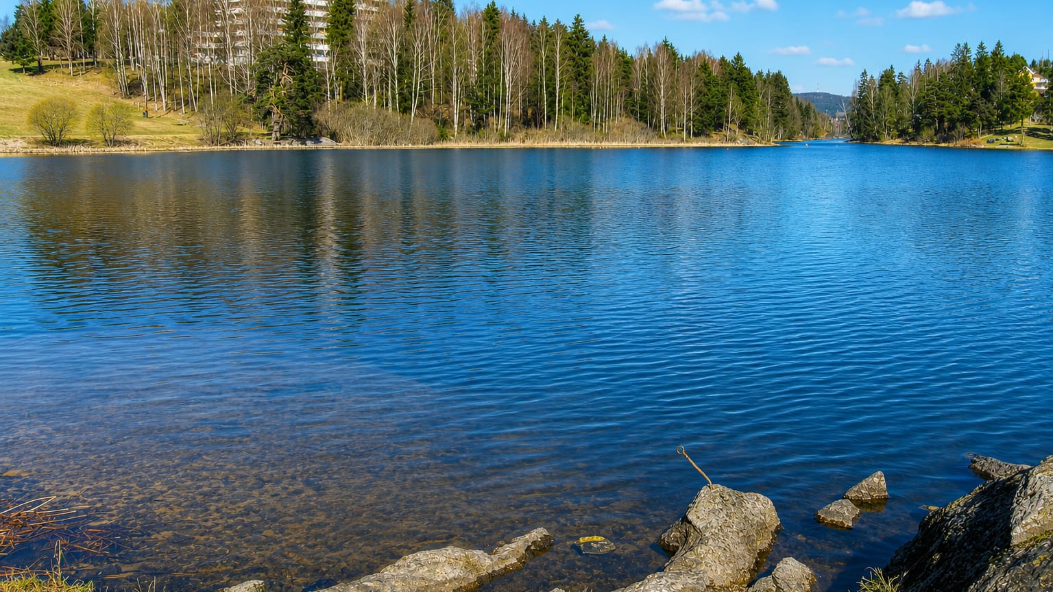 A calm forest-ringed lake with a white apartment block on the hillside at Kjenn, Norway.