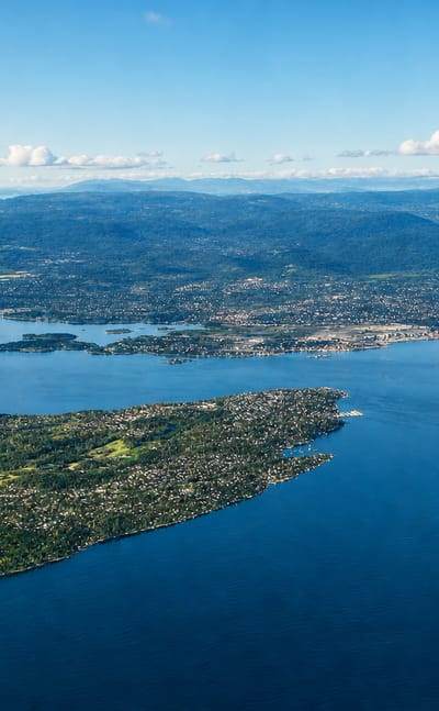 Aerial view of the forested Nesoddtangen peninsula reaching into the blue Oslofjord under a clear sky, Norway.