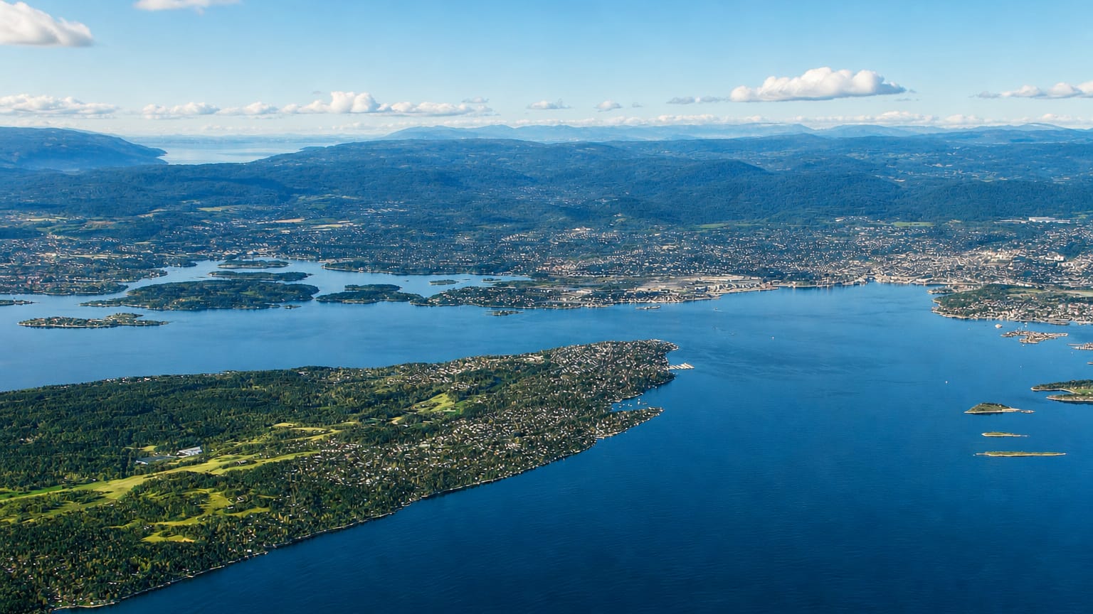 Aerial view of the forested Nesoddtangen peninsula reaching into the blue Oslofjord under a clear sky, Norway.
