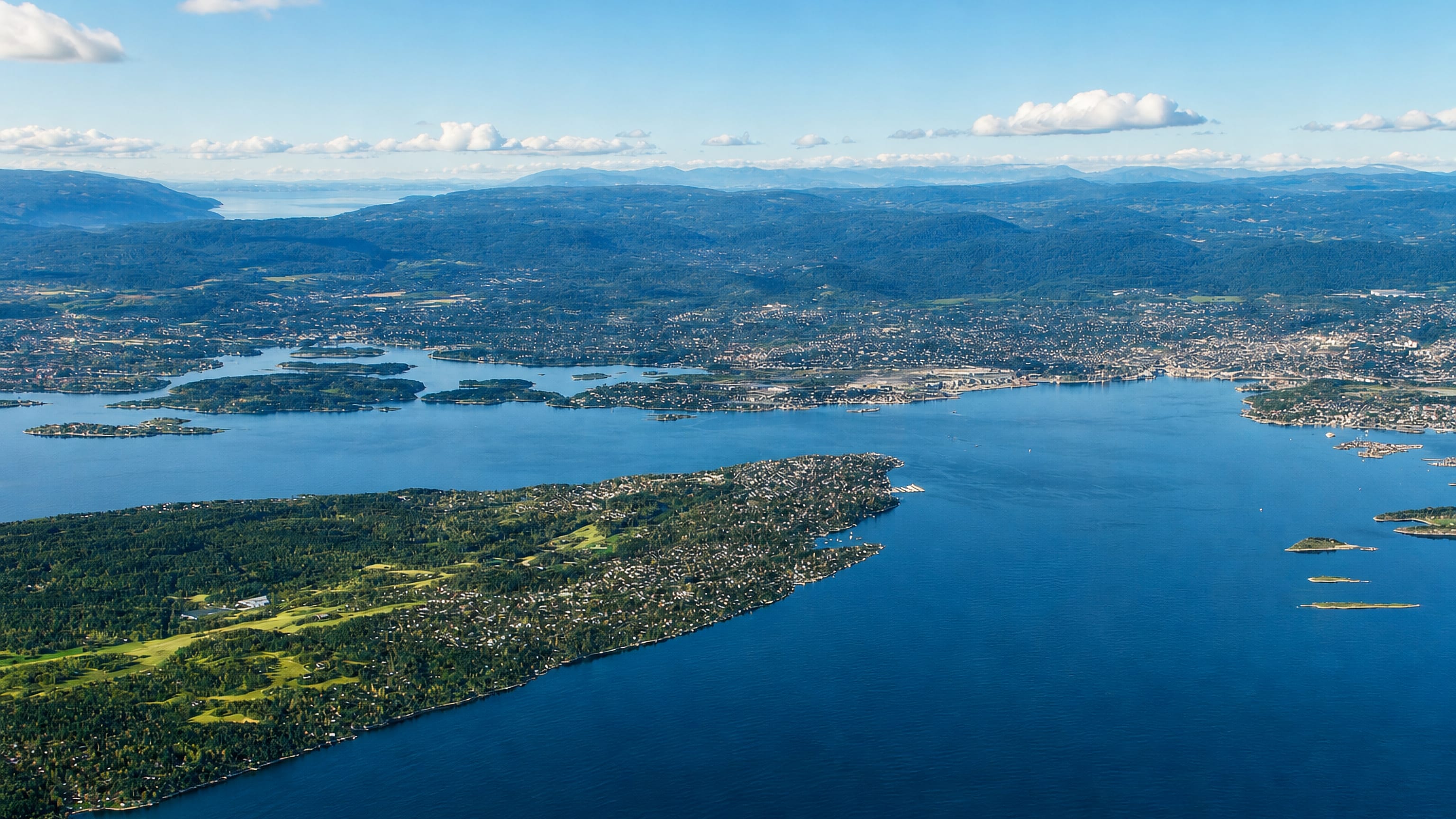 Aerial view of the forested Nesoddtangen peninsula reaching into the blue Oslofjord under a clear sky, Norway.
