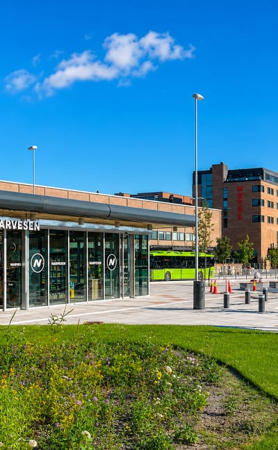 Modern town-centre plaza with a Narvesen kiosk, a green city bus and a brick office block in Ski, Norway.