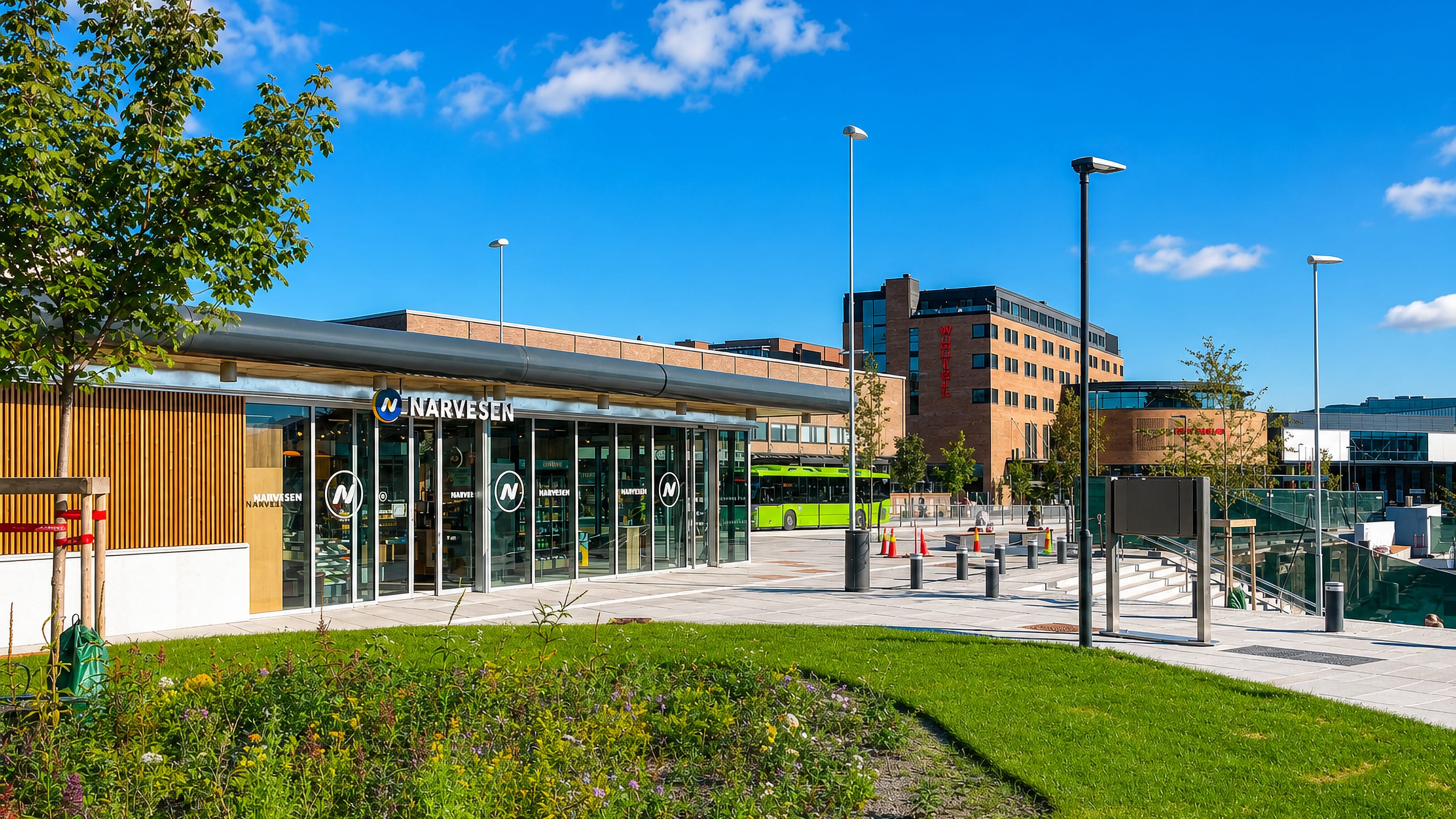 Modern town-centre plaza with a Narvesen kiosk, a green city bus and a brick office block in Ski, Norway.