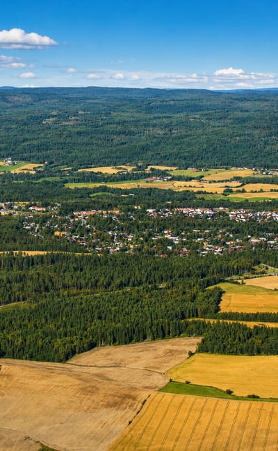 Aerial view of Teigebyen's houses set among farmland and forested hills in Akershus, Norway.