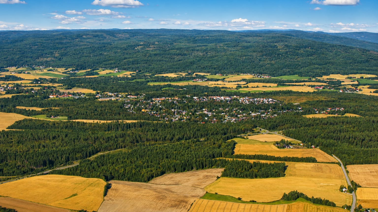 Aerial view of Teigebyen's houses set among farmland and forested hills in Akershus, Norway.