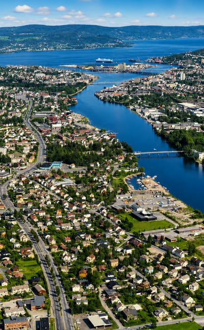 Aerial view of Åssiden, Drammen, with homes along the Drammenselva river winding past forested hills toward the fjord