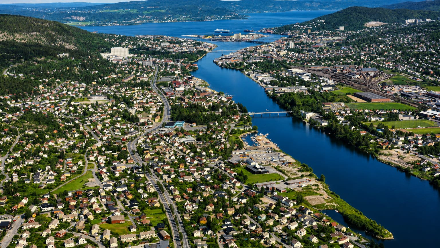 Aerial view of Åssiden, Drammen, with homes along the Drammenselva river winding past forested hills toward the fjord