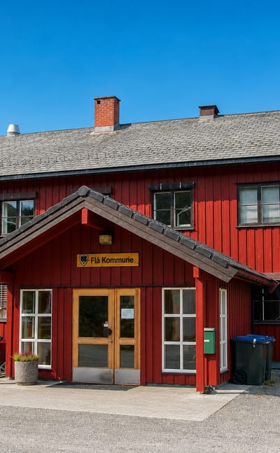 The red timber Flå Kommune municipal building with its name sign, set against forested mountains in Flå, Norway.