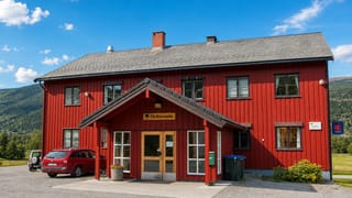 The red timber Flå Kommune municipal building with its name sign, set against forested mountains in Flå, Norway.