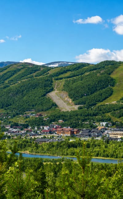 Geilo town centre in a green summer valley below forested mountains with ski slopes and a river, Norway.